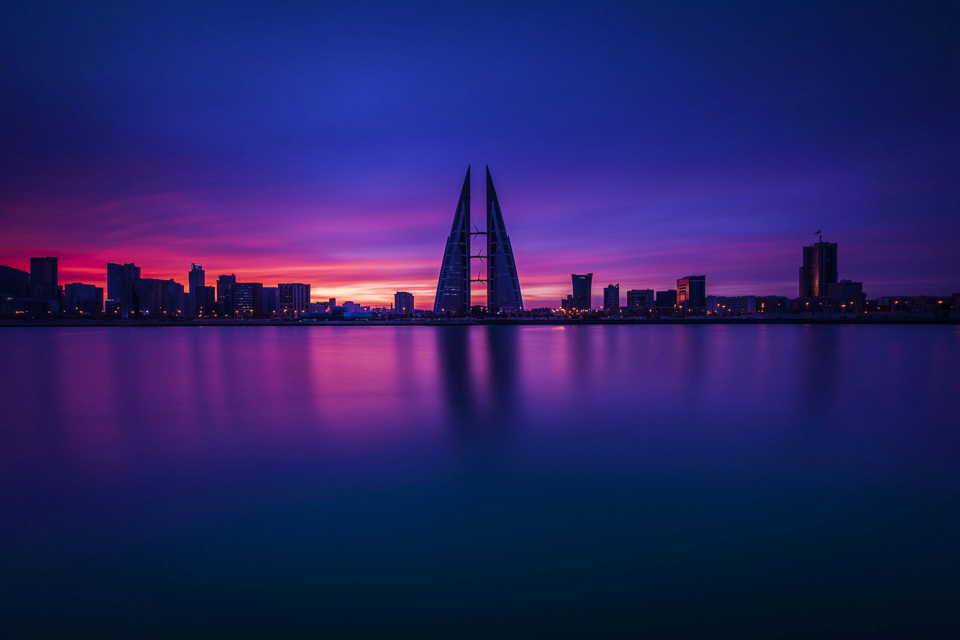 Bahrain Visa Bahrain World Trade Center silhouetted against vibrant purple and pink sunset sky reflected in calm waterfront at dusk